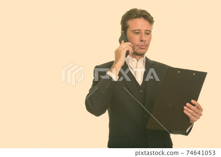 Handsome Caucasian businessman talking on mobile phone while reading clipboard 74641053