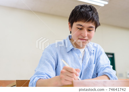 A male university student who takes a lecture in a university classroom and copies a board book into a notebook. A male university student who takes a lecture in a university classroom and copies a board book into a notebook. 74641742