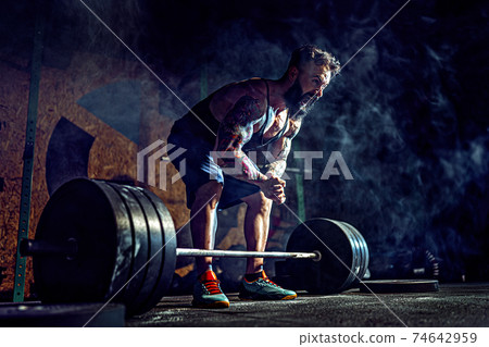 Muscular fitness man preparing to deadlift of a barbell in modern fitness center. Functional training. 74642959