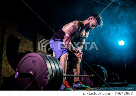 Muscular fitness man preparing to deadlift of a barbell in modern fitness center. Functional training. 74642967