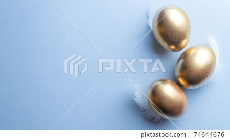 Easter eggs basket. Golden egg in basket with white feathers on pastel blue background in Happy Easter decoration. Traditional decoration in sun light. Top view. 74644676