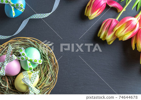 Easter eggs isolated. Colorful egg with tape ribbon, spring tulips on dark rough stone background in Happy Easter decoration. Flat lay, top view. Easter eggs isolated. Colorful egg with tape ribbon, spring tulips on dark rough stone background in Happy Easter decoration. Flat lay, top view. 74644678