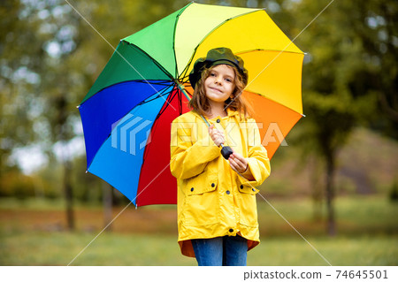 Happy funny child girl with multicolor umbrella in rubber boots at autumn park 74645501