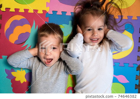 childhood, family friendship, games - close up portrait Two funny joy happy smiling little toddler peschool kids siblings twins brother with sister have fun cover ears playing on mat at home indoors childhood, family friendship, games - close up portrait Two funny joy happy smiling little toddler peschool kids siblings twins brother with sister have fun cover ears playing on mat at home indoors 74646382