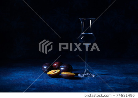 Plum brandy Slivovice in shot glass with fresh ripe plums on blue table with dark background. Plum brandy Slivovice in shot glass with fresh ripe plums on blue table with dark background. 74651496