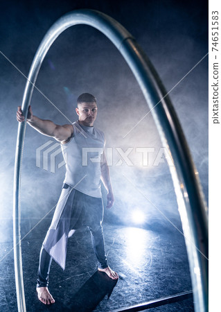 Cyr Wheel circus artist on smoked, dark background performing on stage Cyr Wheel circus artist on smoked, dark background performing on stage 74651583