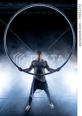 Cyr Wheel circus artist on smoked, dark background performing on stage Cyr Wheel circus artist on smoked, dark background performing on stage 74651743