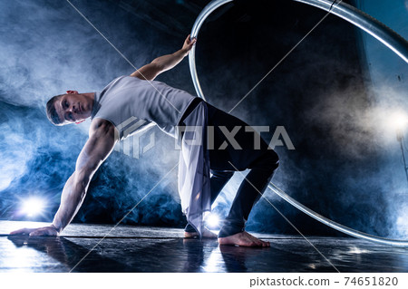 Cyr Wheel circus artist on smoked, dark background performing on stage Cyr Wheel circus artist on smoked, dark background performing on stage 74651820