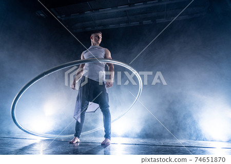 Cyr Wheel circus artist on smoked, dark background performing on stage Cyr Wheel circus artist on smoked, dark background performing on stage 74651870