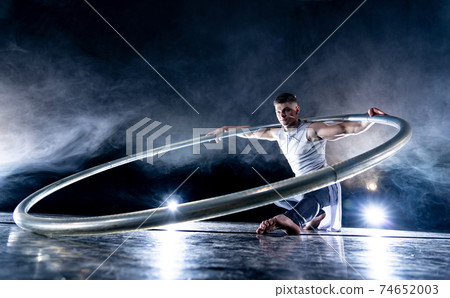 Cyr Wheel circus artist on smoked, dark background performing on stage Cyr Wheel circus artist on smoked, dark background performing on stage 74652003