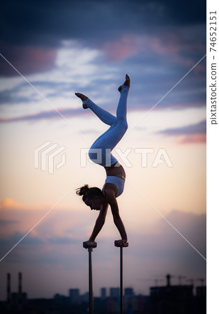 Flexible female circus Artis keep balance and doing contortion on the rooftop against dramatic sunset and cityscape. Motivation, passion and achievement concept  74652151