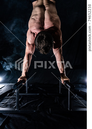 Muscular build man doing crossfit on parallels bar indoor on black, smoked background. concept of healthy lifestyle and calisthenic 74652238