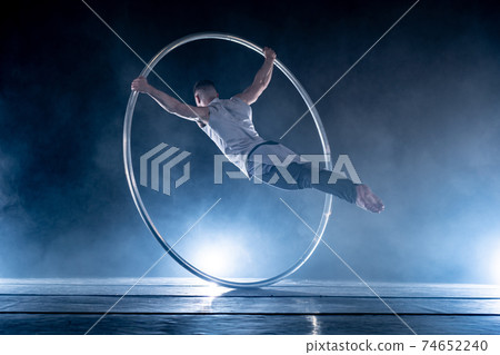 Cyr Wheel circus artist on smoked, dark background performing on stage Cyr Wheel circus artist on smoked, dark background performing on stage 74652240