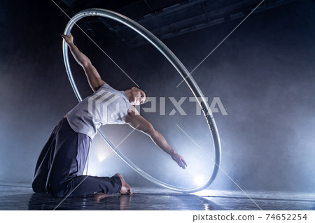 Cyr Wheel circus artist on smoked, dark background performing on stage  74652254