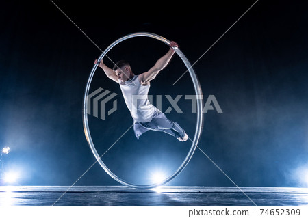 Cyr Wheel circus artist on smoked, dark background performing on stage Cyr Wheel circus artist on smoked, dark background performing on stage 74652309