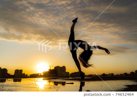 Silhouette Flexible female dancer making trick with reflection in the water during dramatic sunset. Concept of happiness and healthy lifestyle Silhouette Flexible female dancer making trick with reflection in the water during dramatic sunset. Concept of happiness and healthy lifestyle 74652464