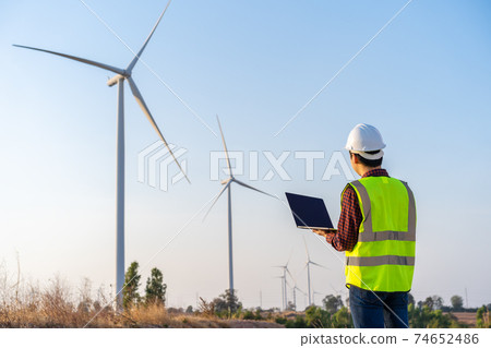 male engineer working with laptop computer against wind turbine farm male engineer working with laptop computer against wind turbine farm 74652486