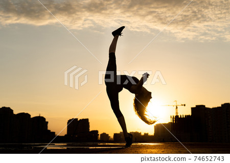 Female dancer showing her flexibility during sunset on cityscape background with reflection in the water. Concept of willpower and opportunity Female dancer showing her flexibility during sunset on cityscape background with reflection in the water. Concept of willpower and opportunity 74652743