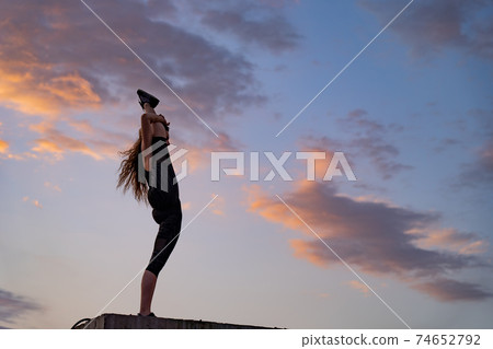 Flexible female dancer on the edge of rooftop on the dramatic sky background during sunset . Concept of healthy lifestyle, talent and aspiration 74652792