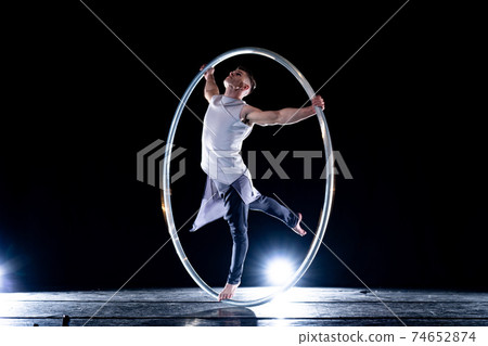 Cyr Wheel circus artist on smoked, dark background performing on stage  74652874