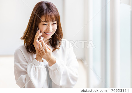 A woman who puts her smartphone on her ear and smiles A woman who puts her smartphone on her ear and smiles 74653524