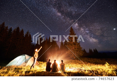 Male is showing his friends Milky Way over camping. Outdoor recreation 74657623