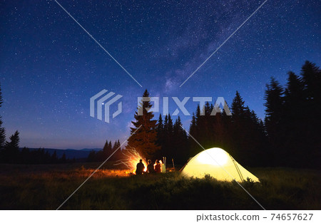 Tourists sitting near campfire under starry sky. 74657627