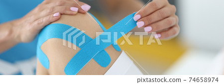 Traumatologist holds blue tape in his hand to fix patient's knee joint in clinic Traumatologist holds blue tape in his hand to fix patient's knee joint in clinic 74658974