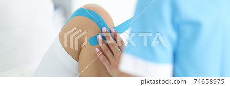 Traumatologist conducts taping of patient's leg in hospital closeup Traumatologist conducts taping of patient's leg in hospital closeup 74658975