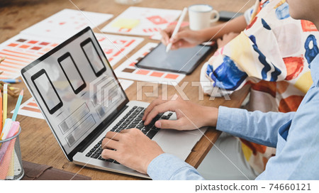 Cropped image of two people is using a computer laptop with an interface icon on the screen at the wooden table. Cropped image of two people is using a computer laptop with an interface icon on the screen at the wooden table. 74660121