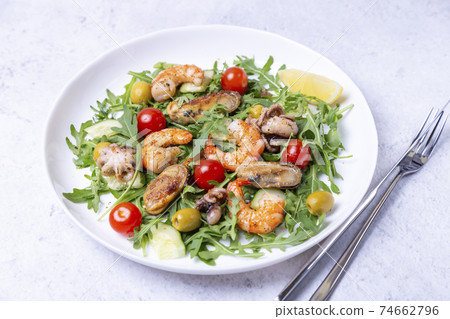 Salad with seafood, arugula, tomatoes, cucumbers and olives on a white plate. Close-up. 74662796
