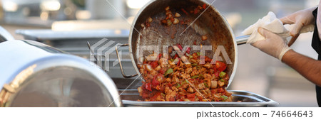 Man put cooked food from frying pan into metal container. 74664643