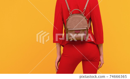 Young girl in a red suit with a small backpack on a yellow background Young girl in a red suit with a small backpack on a yellow background 74666365