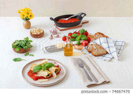 Cannelloni stuffed with spinach, feta cheese and cashew nuts with tomato and garlic sauce, embellished with parmesan cheese shavings and basil leaves. All on white wooden table background. 74667470