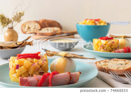 Henri Egg, tasty fresh brunch or snack. Henri Egg, tasty brunch or snack. Boiled eggs and smoked sprats fish with mayonnaise, ham and potato salad. White wooden table, no people. 74668833