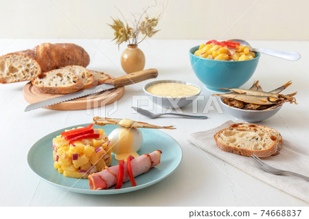 Henri Egg, tasty fresh brunch or snack. Henri Egg, tasty brunch or snack. Boiled eggs and smoked sprats fish with mayonnaise, ham and potato salad. White wooden table, no people. 74668837
