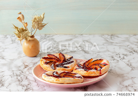 Plate with plum tarts with cinnamon and icing sugar on the table, tasty puff pastry dessert. 74668974