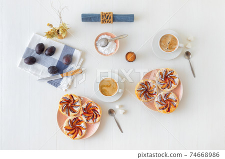 Plate with plum tarts with cinnamon and icing sugar on white wooden table, tasty puff pastry dessert. 74668986