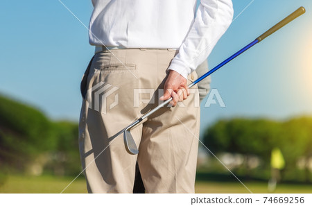 On focus shot of back of a golfer holding a club on a green golf field. The background is out of focus, creating a nice aesthetic. On focus shot of back of a golfer holding a club on a green golf field. The background is out of focus, creating a nice aesthetic. 74669256