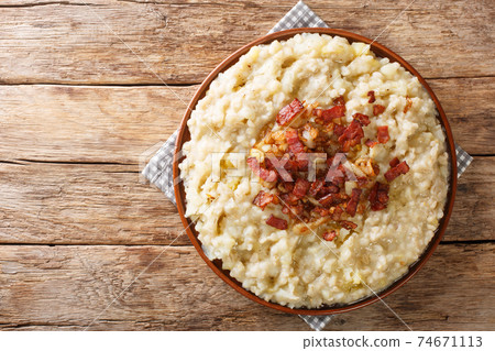 Potato and pearl barley porridge and bacon with fried onion closeup in the plate. Horizontal top view 74671113