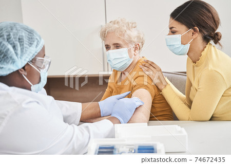 Woman looking at a multiracial doctor vaccinating her 74672435