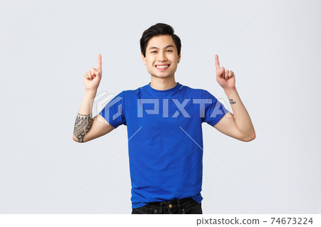 Different emotions, people lifestyle and advertising concept. Cheerful handsome asian man in blue t-shirt pointing fingers up. Guy advertising and inform about new promo, smiling camera 74673224