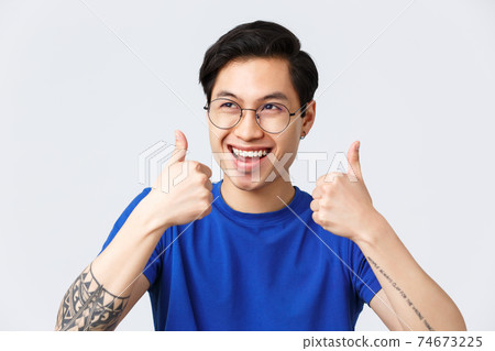 Lifestyle, people emotions and beauty concept. Enthusiastic happy asian man in glasses, smiling upbeat looking away, showing thumbs-up in approval, have greay idea, enjoying plan 74673225