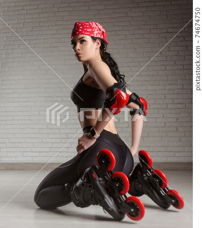 a slender woman in sportswear on roller skates is sitting on the floor 74674750