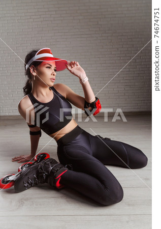 a slender woman in sportswear on roller skates is sitting on the floor 74674751
