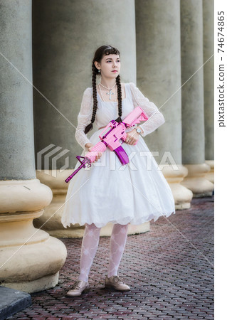 Girl in a white dress with a pink rifle plays airsoft Girl in a white dress with a pink rifle plays airsoft 74674865