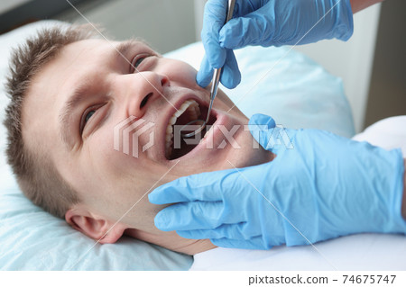 Dentist examining oral cavity of male patient with mirror 74675747
