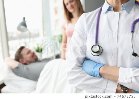 Doctor standing with his arms crossing on background of sick patient 74675753