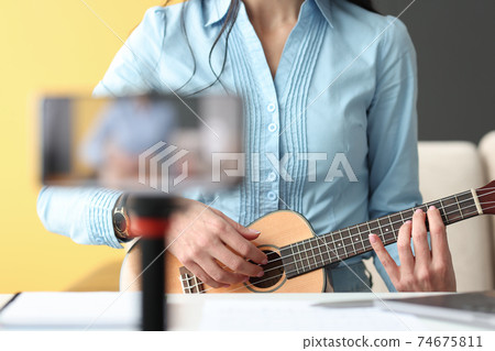 Woman playing ukulele and filming phone closeup Woman playing ukulele and filming phone closeup 74675811