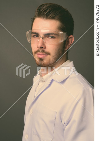 Young handsome bearded man doctor wearing protective glasses against gray background Young handsome bearded man doctor wearing protective glasses against gray background 74676272